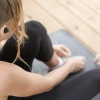 woman in workout gear, sits on a yoga mat and ties her shoe