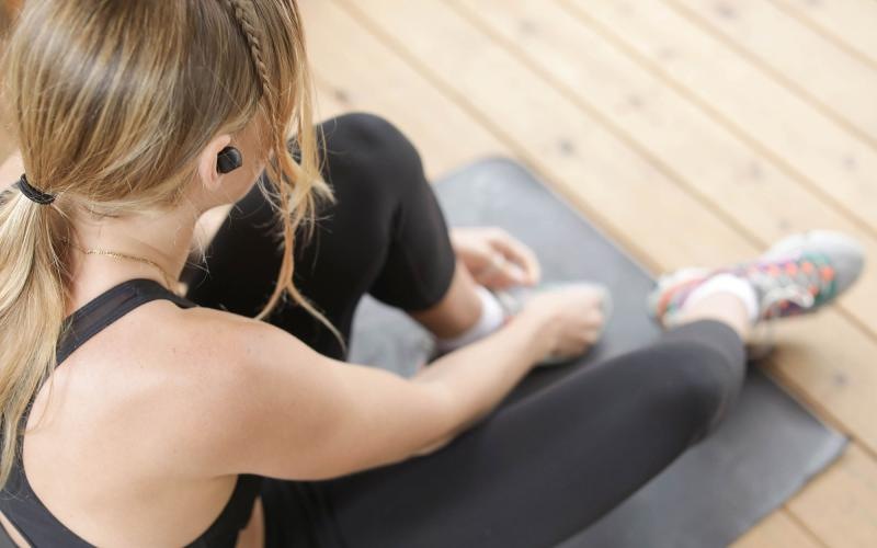 woman in workout gear, sits on a yoga mat and ties her shoe